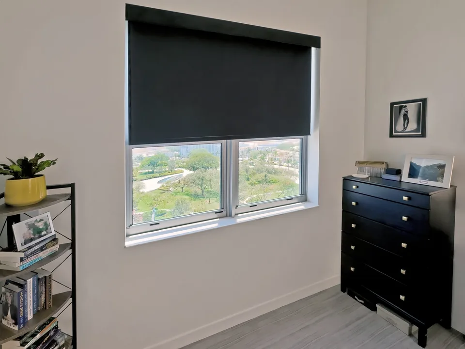 Dark opaque Insolroll blackout roller shade partially lowered over a bedroom window